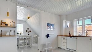 Una cocina luminosa con armarios blancos, encimera de madera y una zona de comedor con sillas blancas.