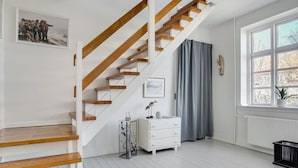Una escalera con escalones de madera y una pared blanca. Se ve una ventana con vistas a árboles y una planta en el alféizar.