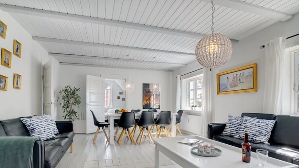 Una sala moderna con comedor, que presenta techo blanco, sofás de cuero negro, una mesa de centro blanca y una araña.