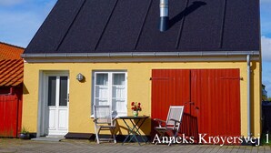 Un bâtiment jaune avec un toit noir, une porte rouge et une cheminée.