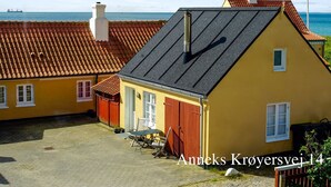Un bâtiment jaune avec un toit rouge, une cheminée et une petite fenêtre.