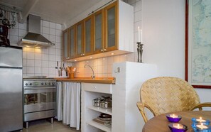 Een moderne keuken met roestvrijstalen apparatuur, houten kastjes en een eethoek met een geweven stoel en een tafel.