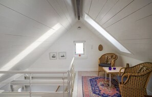 Een zolderkamer met hoge plafonds, een schuine daklijn, een klein raam en uitzicht op de lucht.