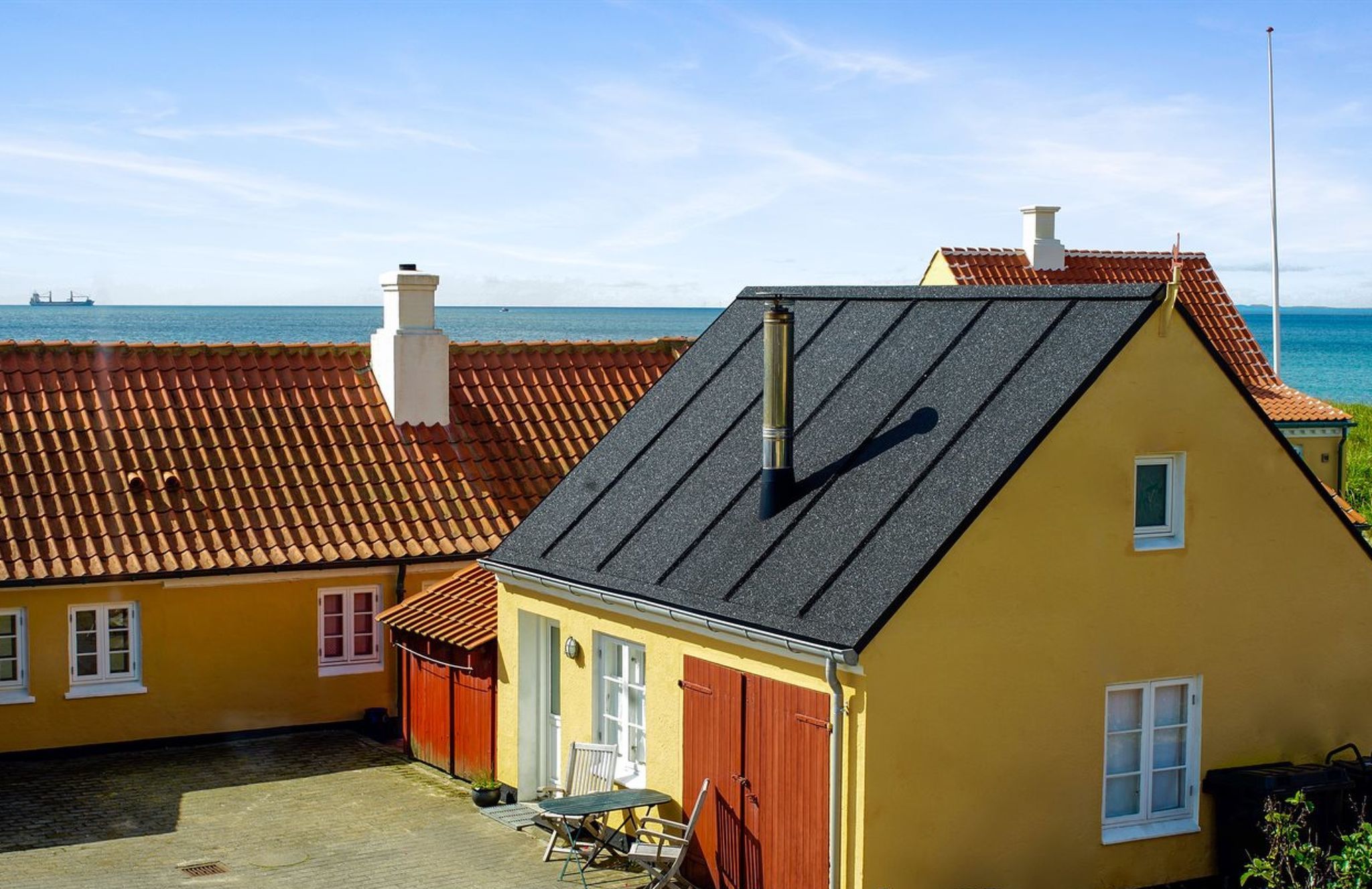 En gul bygning med rødt tag, skorsten og et lille vindue.