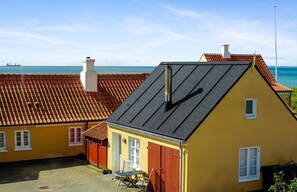 Een geel gebouw met een rood dak, schoorsteen en een klein raam.