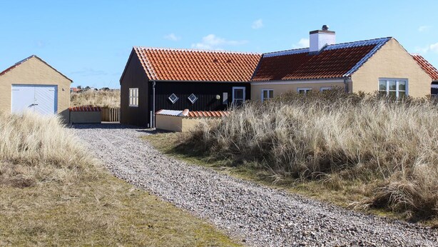 Casa rural con camino de grava y hierba alta alrededor.