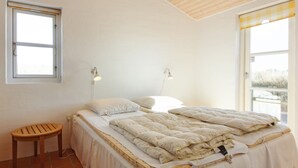 Un dormitorio con cama, dos lámparas de noche, un taburete de madera y una ventana.