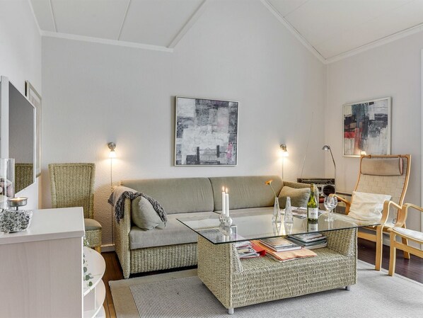 A modern living room with a sofa, a glass coffee table, and a chair. There are two wall-mounted lamps and a framed abstract painting above the sofa.