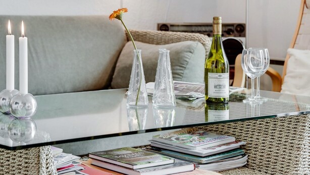 Ein Tisch mit Glasplatte, eine Weinflasche, zwei Kerzen und eine Vase mit einer Blume.