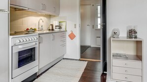 Eine moderne Küche mit weißen Schränken, einem Herd und einem Spülbecken. Auf dem Boden liegt ein kleiner Teppich und eine Tür führt in einen weiteren Raum.