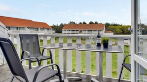Ein Balkon mit zwei Stühlen, einem Tisch, einer Weinflasche und einem Blumentopf.