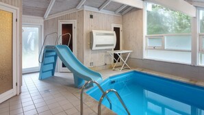 An indoor swimming pool with a blue slide, a small table, and a sauna.