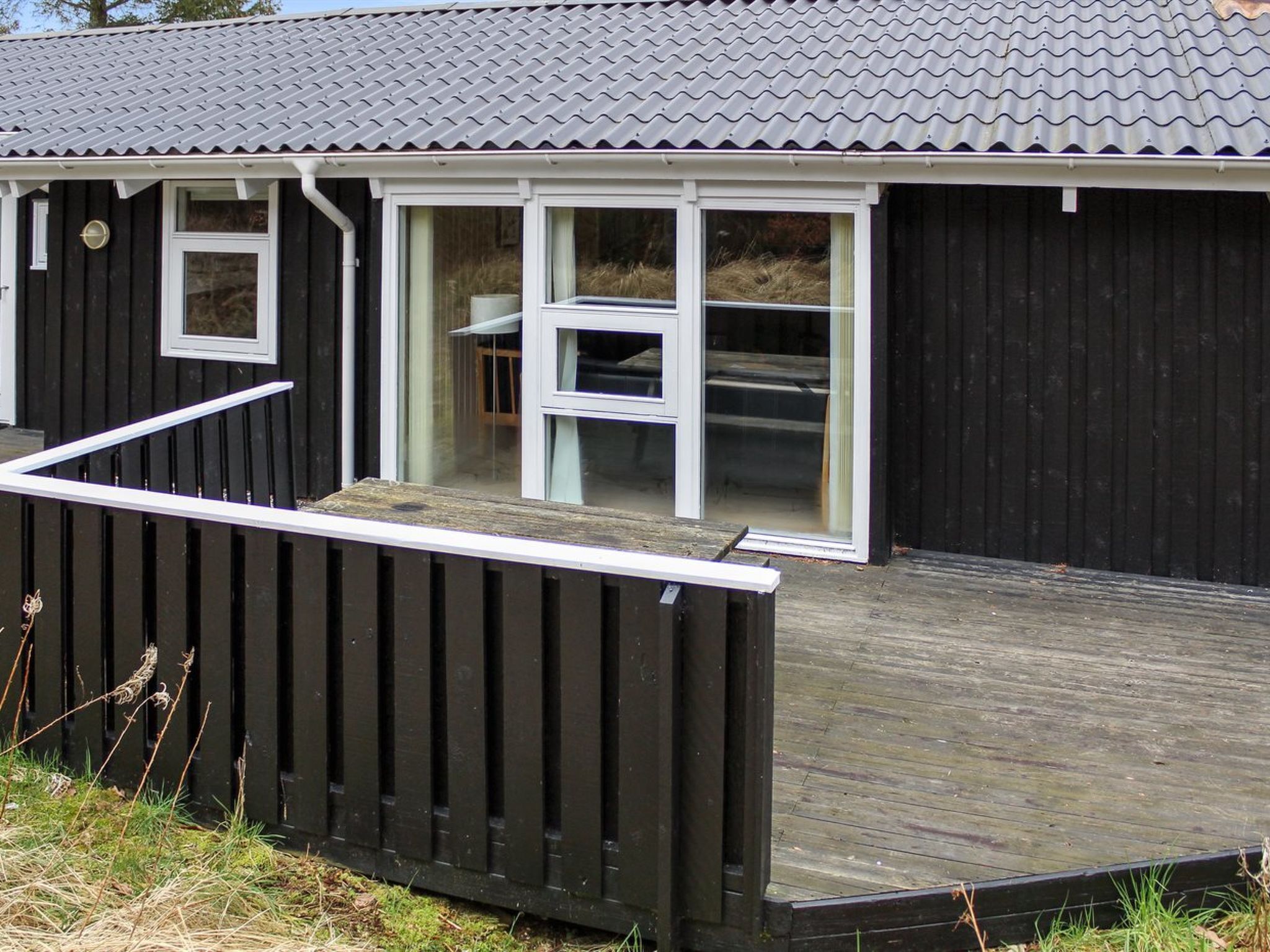 En moderne bygning med mørkt ydre, træterrasse og store vinduer.