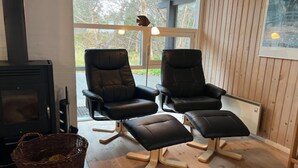 A cozy room with two black leather chairs and a matching ottoman, a fireplace, and a large window with a view of trees.