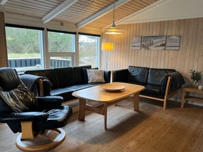 Ett rum med trägolv, en svart lädersoffa, ett träbord och en hängande lampa.