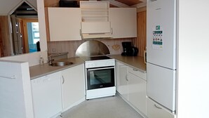 Cocina compacta con armarios blancos, estufa de acero inoxidable, horno integrado, lavamanos y refrigerador blanco.