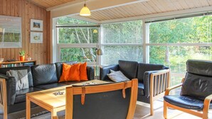 Een gezellige woonkamer met een houten plafond, een zwart lederen bank, een houten salontafel en uitzicht op groen.