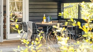 An outdoor dining area with a wooden table and chairs, a bottle of olive oil, and a pitcher.