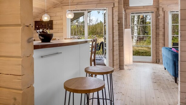 A wooden cabin with a kitchen area featuring a bar counter, two stools, and pendant lighting.