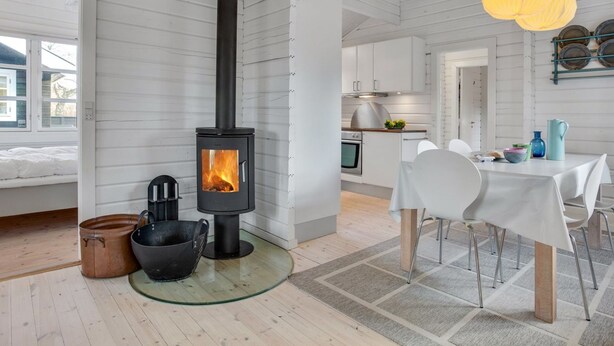 A modern kitchen with a central wood-burning stove, a dining area with a table and chairs, and a visible kitchen counter with appliances. - "Dorthea" - 200m from the sea by Interhome (Jerup)