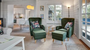 A cozy living room with two green armchairs, a white coffee table, and a view of a kitchen and dining area through large windows. - "Dorthea" - 200m from the sea by Interhome (Jerup)
