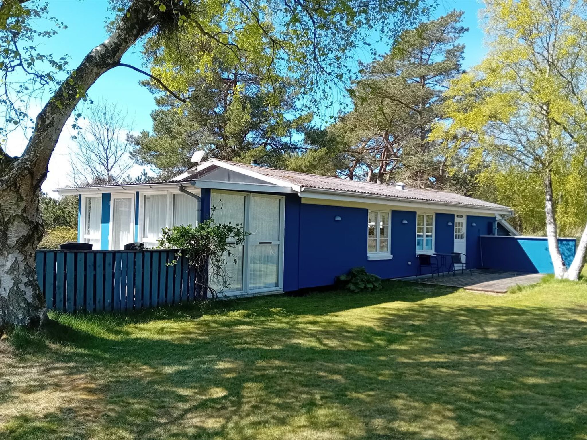 Einbungalow mit blauer Fassade, einer überdachten Veranda und einem umzäunten Garten.