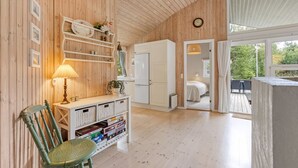 Een gezellige kamer met houten wanden, een witte deur, een eethoek met een tafel en stoelen, en een boekenplank met diverse voorwerpen.