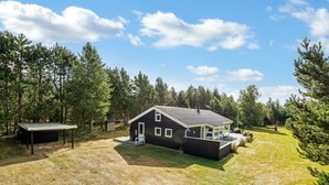 Een modern huis met twee verdiepingen en een groot terras, gelegen in een gazon met een dicht bos eromheen.
