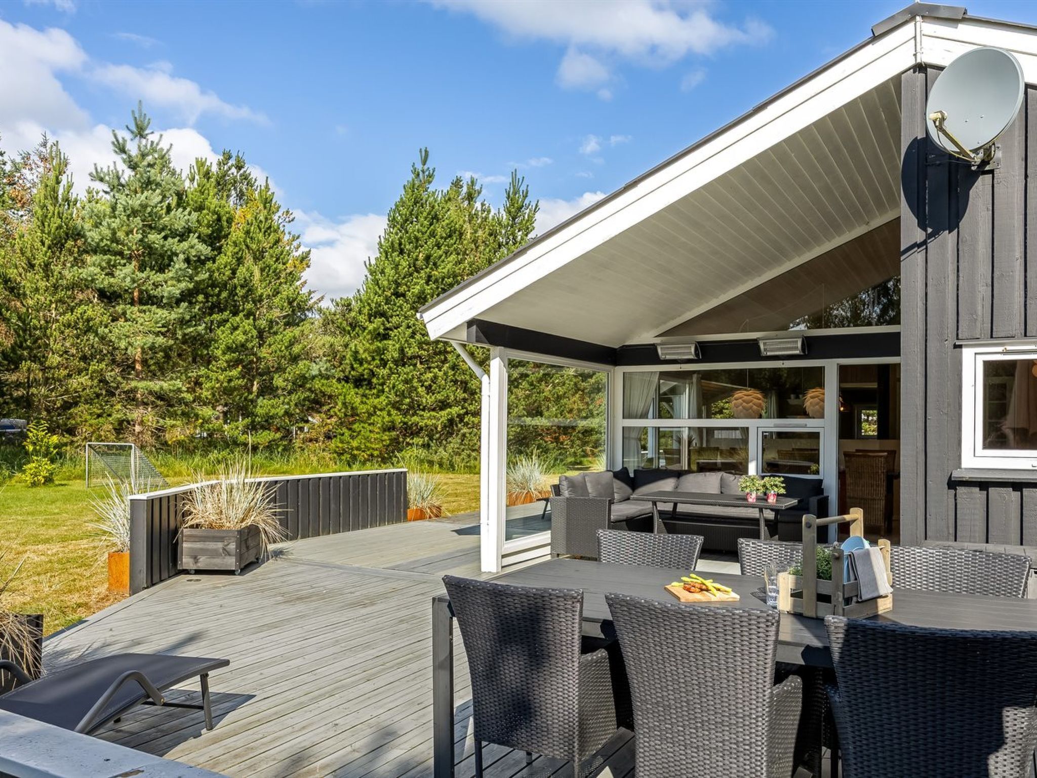 Un patio moderno all'aperto con zona pranzo, area relax coperta e vista su un paesaggio boschivo.