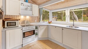 Een moderne keuken met witte kasten, een ingebouwde oven, een magnetron en een groot raam met uitzicht op de omgeving.