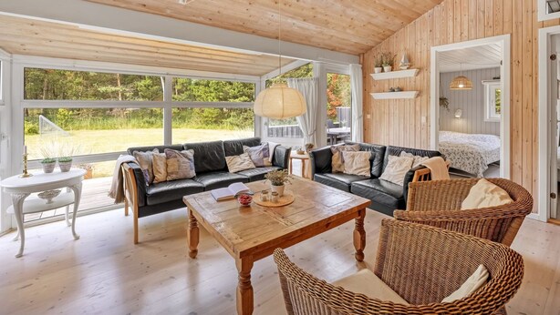 Een ruime woonkamer met een houten plafond, een grote bank, een salontafel en rieten stoelen.