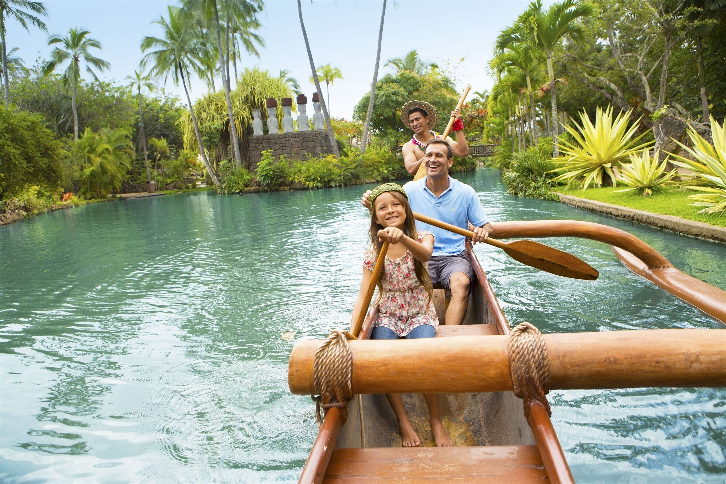A traditional canoe with passengers on a calm river surrounded by lush greenery and palm trees.