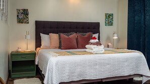 A neatly made bed with a white quilt, multiple pillows, and a decorative headboard. - "Pua Pono House" | Pupukea Acerage, Fruit Trees (Haleiwa)