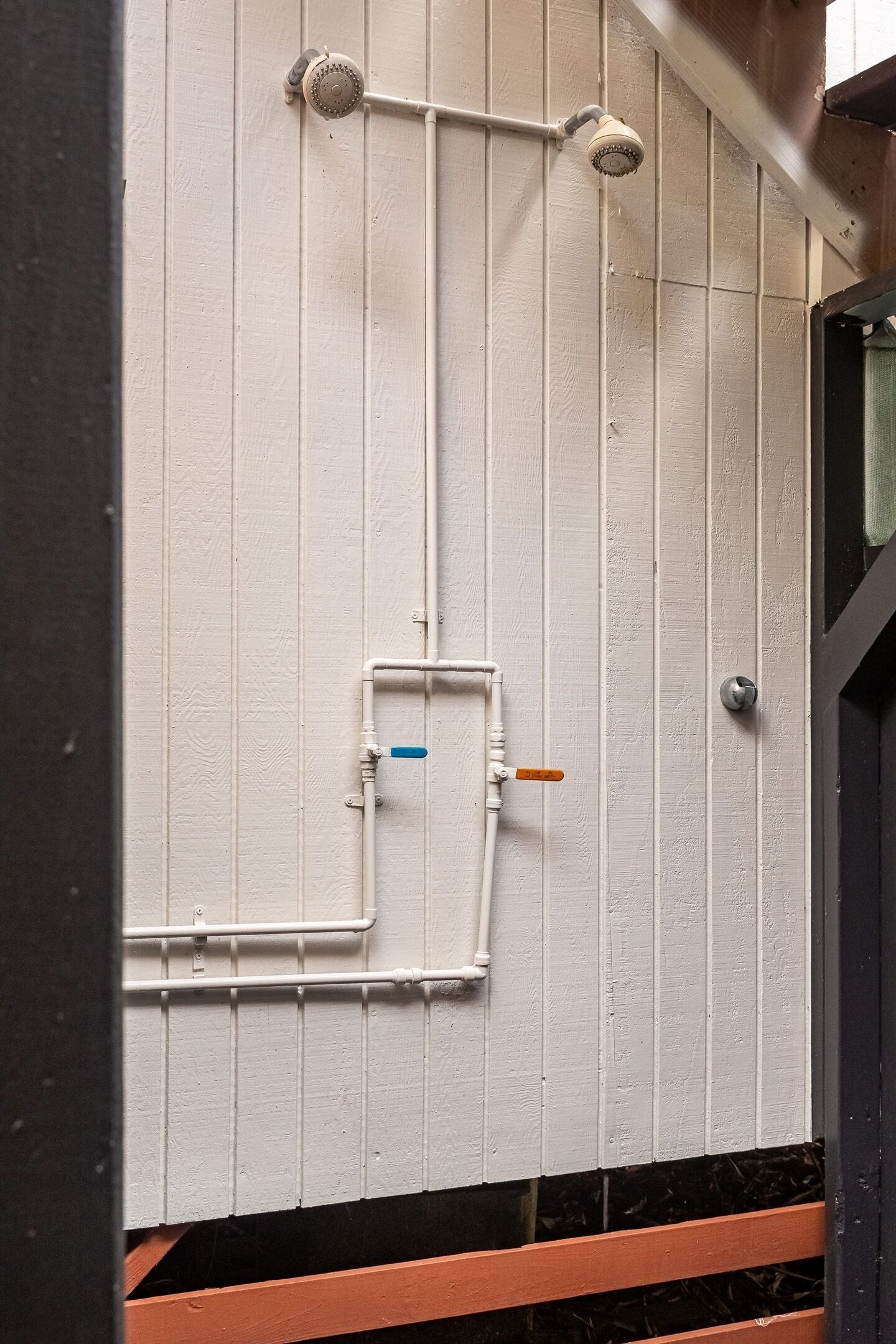 A white wall with a showerhead, a pipe, and a valve.