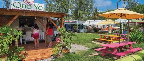 Un patio de comidas al aire libre con un letrero que dice 'Qno Yo', un puesto de comida tailandesa llamado 'Thongs Thai' y mesas de picnic.