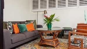 A living room with a grey sofa, colorful cushions, a round wicker coffee table, a green plant, and a patterned armchair. - "Pua Pono House" | Pupukea Acerage, Fruit Trees (Haleiwa)