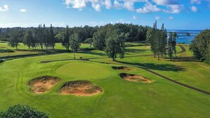 A golf course with bunkers, trees, and a view of the ocean. - "Pua Pono House" | Pupukea Acerage, Fruit Trees (Haleiwa)