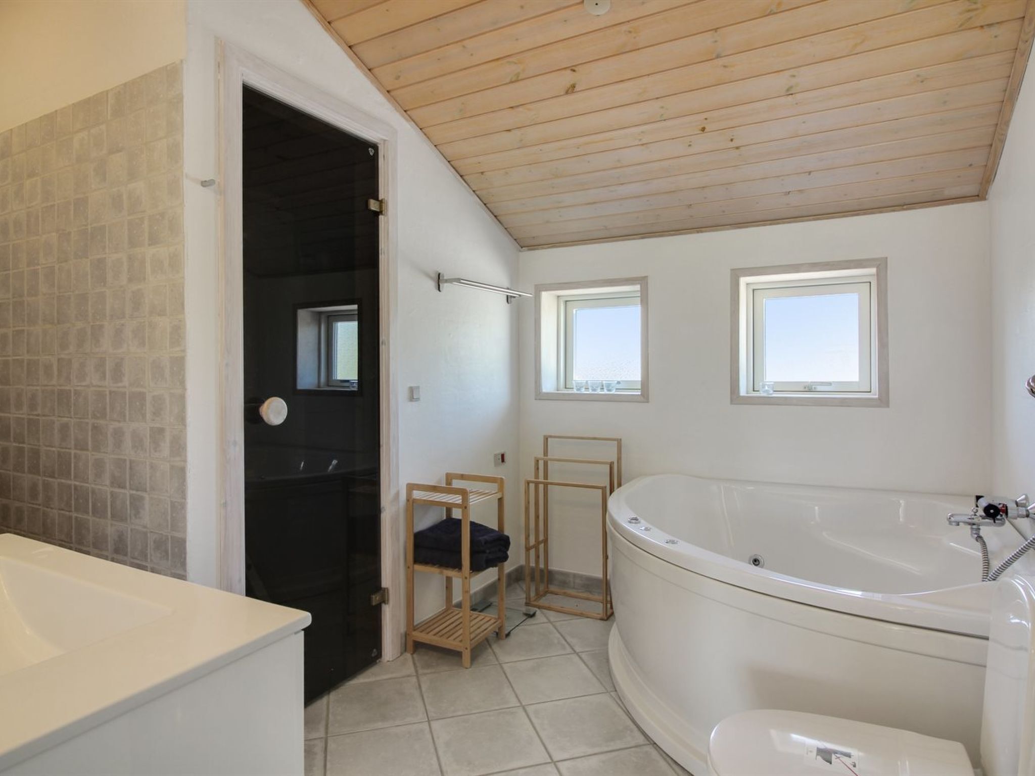 Ein Badezimmer mit Badewanne, Toilette und Waschbecken. Zwei Fenster sorgen für natürliches Licht.