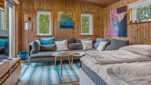 Een gezellig interieur van een chalet met een bank, een bed, een kleine tafel en kunst aan de wanden.