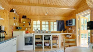 Een houten blokhut van binnen met een keuken, een eethoek en een tv aan de muur.