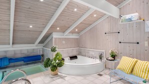 Zona d'una piscina interior moderna amb un banyera d'hidromassatge, una cadira i plantes en testos.
