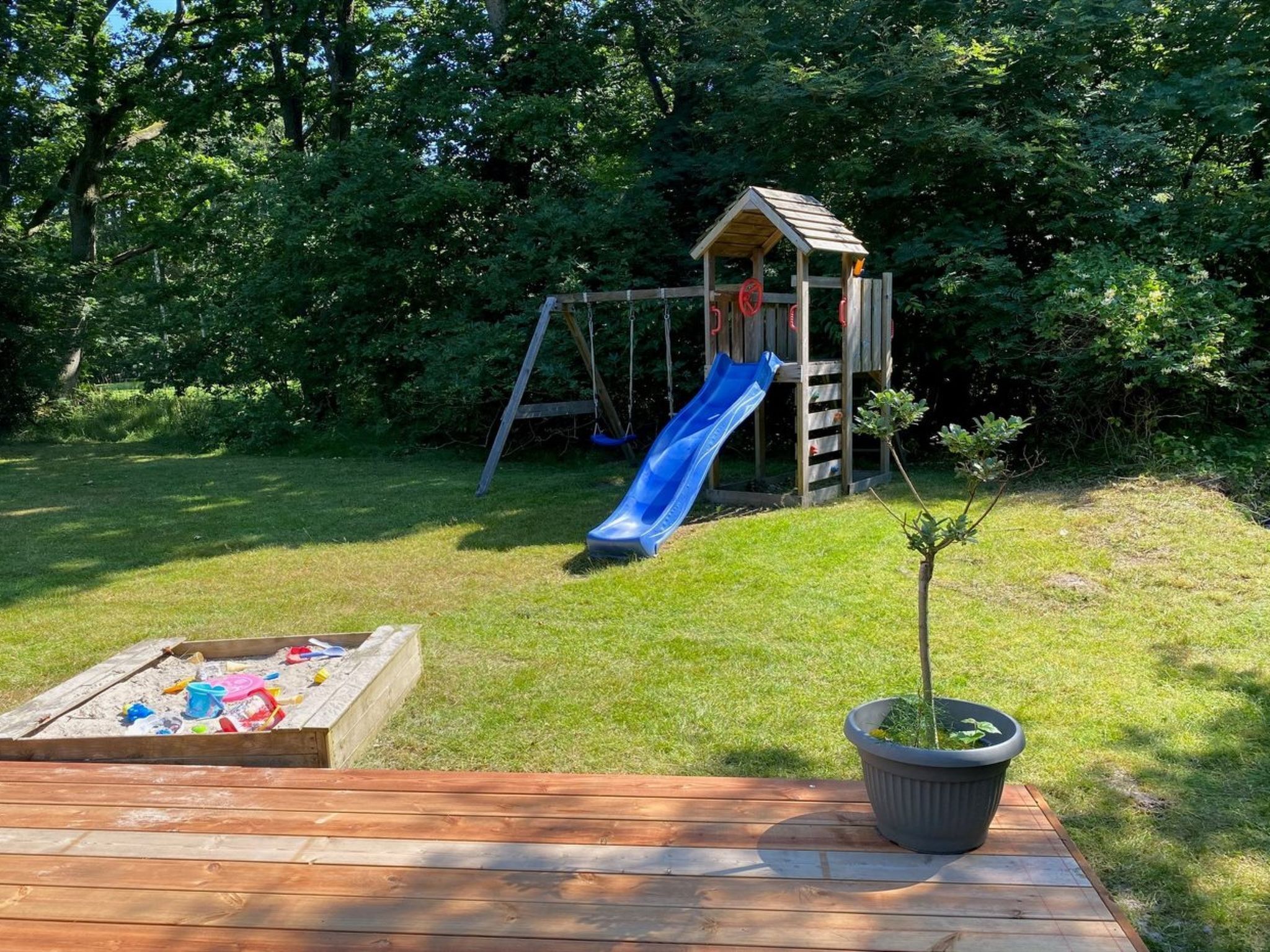 A wooden deck with a sandbox and a potted plant.