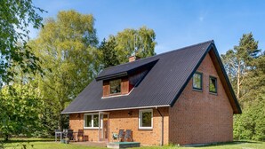 Une maison de plain-pied en briques, avec un toit en pente, une véranda à l’avant avec une table et des chaises, et une petite terrasse.
