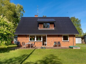Une maison à deux étages, avec un toit sombre, une façade en briques et un porche à l’avant, agrémenté d’une table et de chaises.