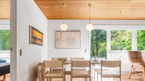 Un espace repas moderne avec un plafond en bois, une carte accrochée au mur et de grandes fenêtres donnant sur un paysage verdoyant.