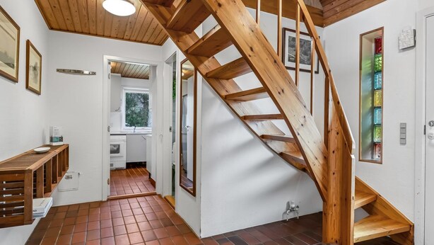 Un intérieur moderne avec un escalier en bois, des murs blancs et un revêtement de sol carrelé.