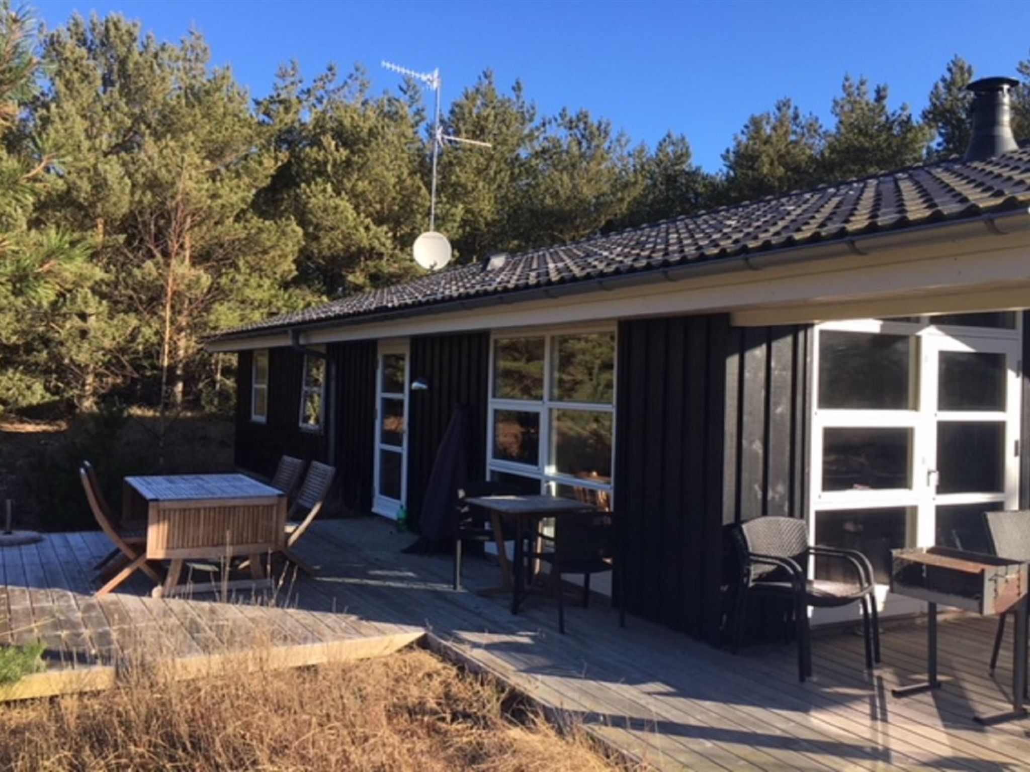 A small house with a patio area, including a table and chairs, surrounded by trees.