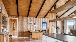 A wooden interior with a dining area, kitchen, and a large window.