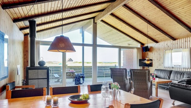 A spacious room with a wooden ceiling, large windows, a dining table with chairs, a sofa, and a television.