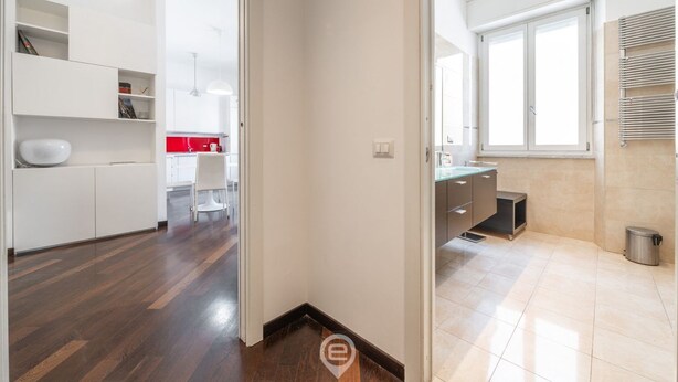 A modern kitchen with white cabinets, a red backsplash, and a large window providing natural light. - Comfort Corner in Via Dante (Cagliari)